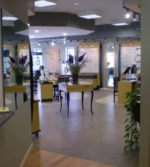 A large shop with various tables, chairs, and a counter, with two people inside and various decorative plants and equipment