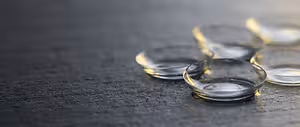 Five contact lenses sit on a dark gray surface, with a slight golden hue on their edges.
