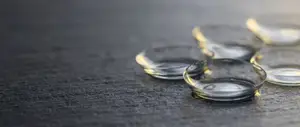 Five contact lenses sit on a dark gray surface, with a slight golden hue on their edges.