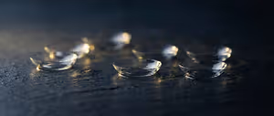A close up of a collection of six contact lenses on a dark surface.