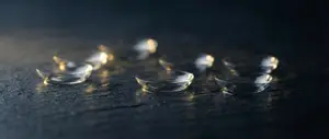 A close up of a collection of six contact lenses on a dark surface.