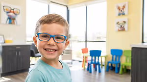 A boy wearing glasses and smiling in a waiting area