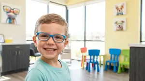 A boy wearing glasses and smiling in a waiting area