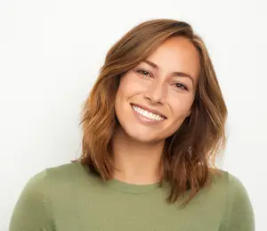 A smiling woman with brown hair wearing a green shirt in a studio