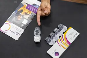 A person pointing at a package of contact lenses and a booklet on a black surface