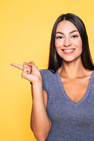 A smiling woman pointing her finger in front of a yellow wall.