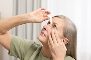 Older woman applying eye drops while looking upward