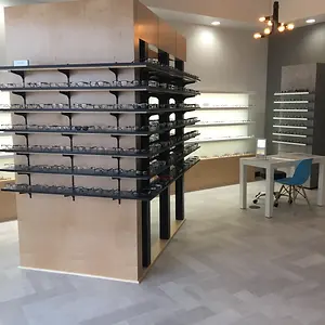 A showroom with a wooden floor, a desk with a blue chair, a display shelf with glasses, and a wall with a gray accent.