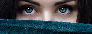 Woman with green eyes peeking through a blue cloth covering her face.