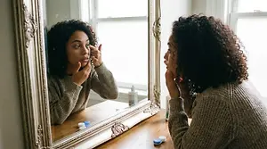 A woman looking at herself in the mirror as she puts in her contacts