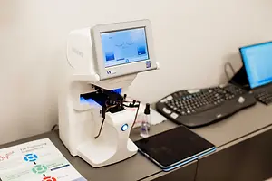 A white device that looks like a machine with a screen and buttons is placed on a table, along with a keyboard, a mouse, and a tablet, with a paper placed in front of the machine.