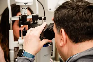 An optometrist uses a slit lamp to examine a patient's eye in an office setting.