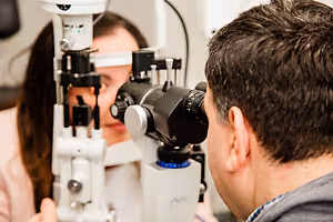 An optometrist is examining a patient's eyes using an ophthalmoscope in an examination room.