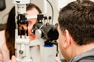 An optometrist is examining a patient's eyes using an ophthalmoscope in an examination room.