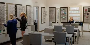 Three women are standing in front of a wall with frames and talking to each other in a store.