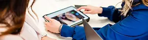 A woman is demonstrating the new Dentrix software on a tablet to another woman who is sitting beside her.