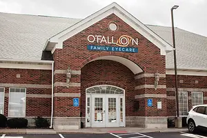 O'Fallon Family Eyecare building exterior with brick walls and glass doors, a white car parked nearby, and a street light on the right side.