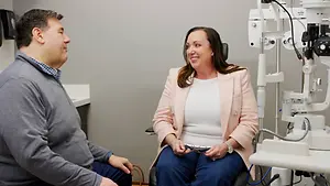 A man and a woman are sitting in front of a machine, probably having an eye checkup in an eye clinic.
