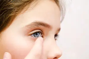 A close up of a young girl putting in a contact lens in her eye.