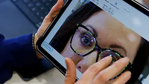 A person holding a tablet with a woman's face on the screen wearing glasses with green lines on them.
