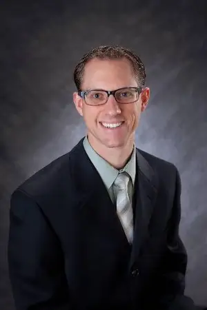 Image of a man in a suit and tie smiling for the camera