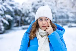 A woman in a blue jacket and white beanie is posing for a photo with her finger on her nose.
