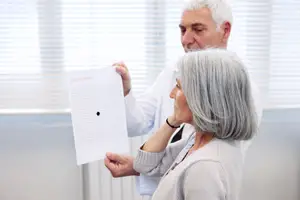 A man and woman in a room, the woman is holding a paper with dots and is looking at it, and the man is looking at her.