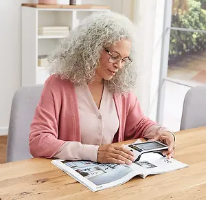 Woman reading a magazine on a table while wearing reading glasses