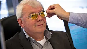 Optometrist adjusting yellow-tinted glasses on an older man