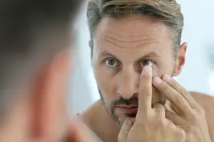 Man looking at his eye in mirror while touching it with fingers
