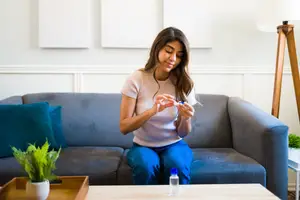 A woman is sitting on a couch and is looking at a contact lens