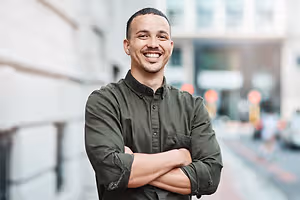 A smiling man with folded arms standing in front of a building on a city street