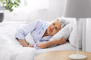 Elderly woman sleeping in bed with white blanket and pillows