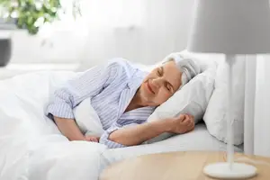 Elderly woman sleeping in bed with white blanket and pillows