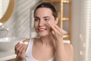 A woman is adjusting her contact lenses in front of a bathroom mirror.