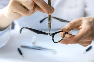 A person using a tool to fix a pair of glasses.