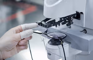 An eyeglass frame being adjusted on a white machine with a lens in front of it.