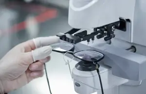 An eyeglass frame being adjusted on a white machine with a lens in front of it.