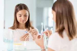 Two girls standing in front of a mirror brushing their teeth