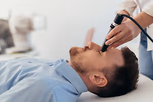 Man lying on a table with a stethoscope on his face being checked by a doctor