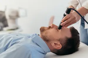 Man lying on a table with a stethoscope on his face being checked by a doctor