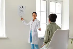 A woman in a white coat is standing and explaining something to a man sitting in front of her in a white chair.
