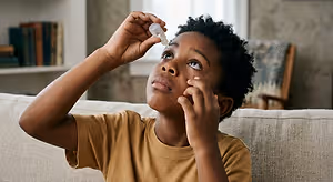 A young boy sitting on a couch and administering eye drops