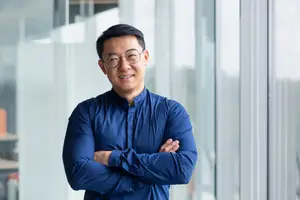 A man standing in front of a glass wall with his arms crossed and smiling