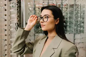 A woman in a suit trying on glasses at an optical store
