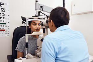 A woman is getting her eyes checked by a man in a blue shirt in a medical clinic.