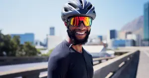 Man in cycling gear standing on a bridge with a city skyline in the background
