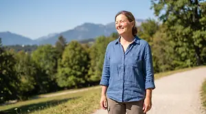 Image of a smiling woman walking down a dirt road surrounded by trees and mountains