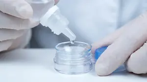 Close up of hands wearing gloves and putting solution into a container for contact lenses.