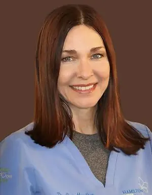 Dr. Erin Hamilton, a female doctor with brown hair wearing a blue coat, is smiling for a portrait.